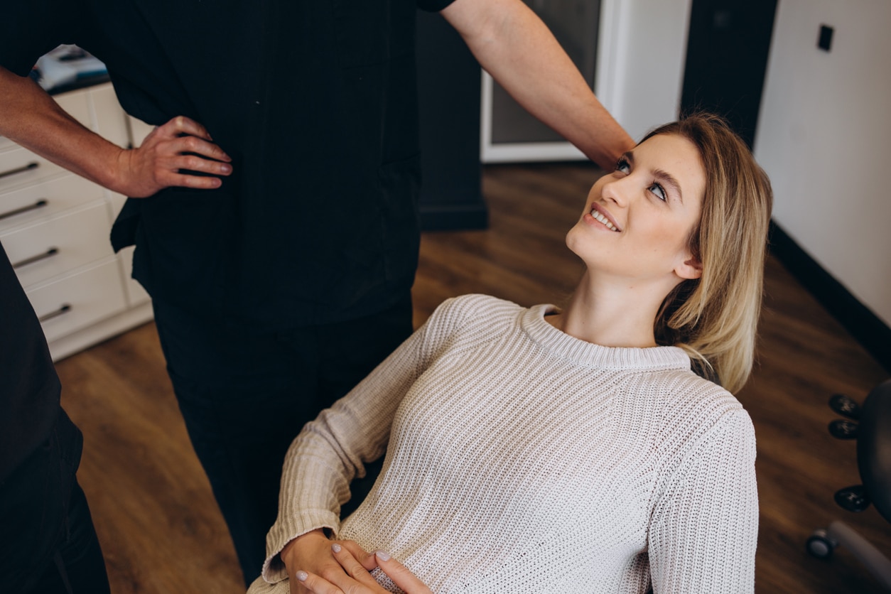 A woman smiling while reclining on a chair, another person standing beside her.