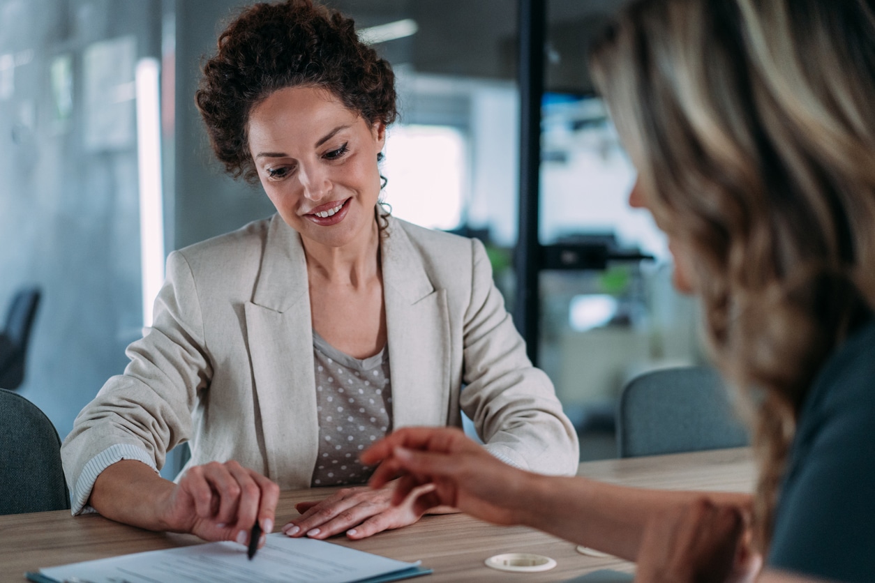 Woman in a blazer discussing paperwork at a meeting table.