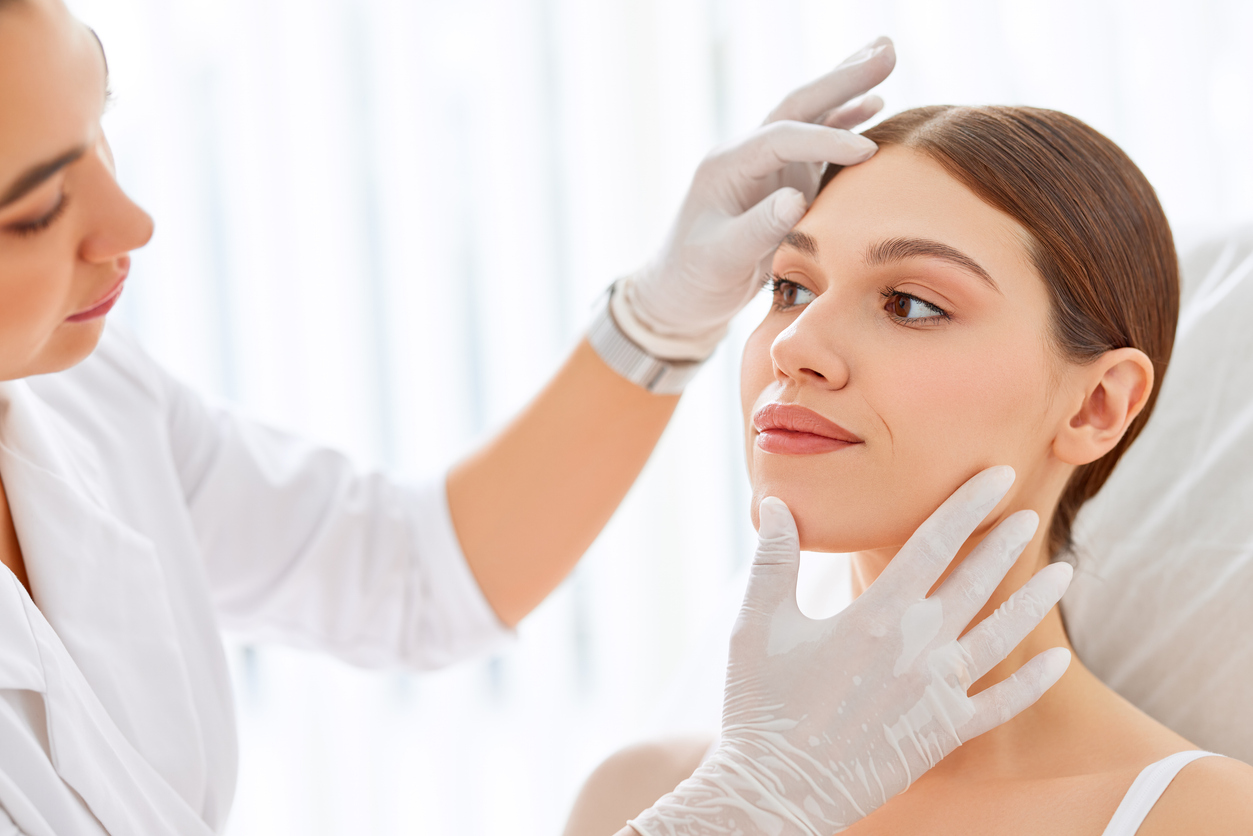 A professional examining a woman's face in a skincare consultation.