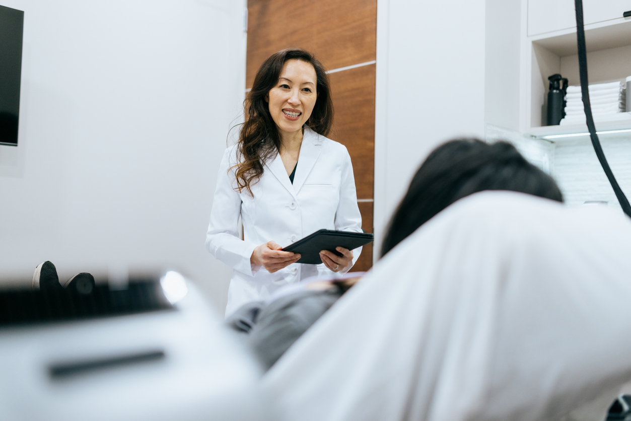 A female doctor holding a tablet speaks to a patient in a medical office.